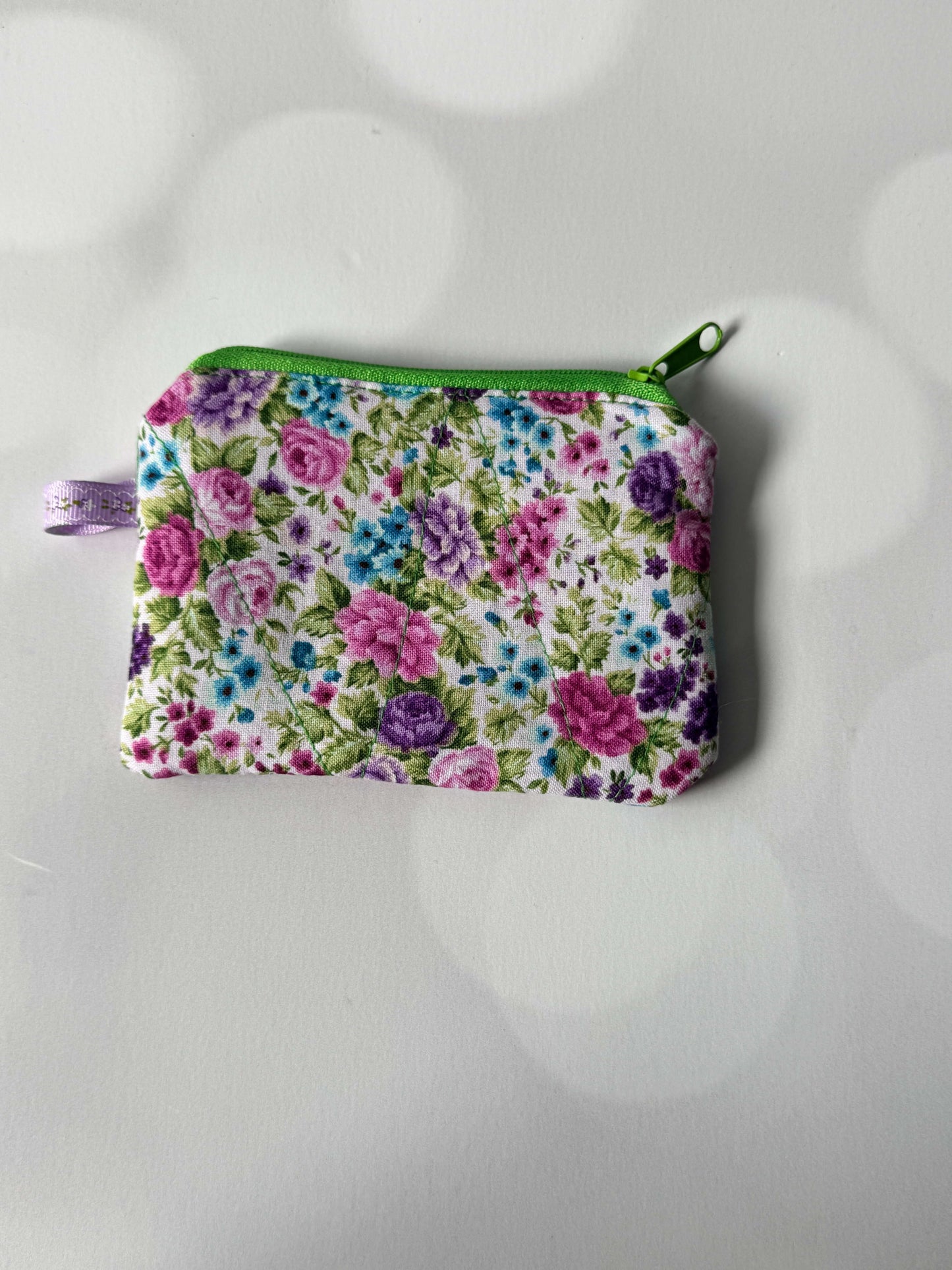 Purple flower coin wallet with a vibrant floral design and green zipper, perfect for carrying coins and small essentials.
