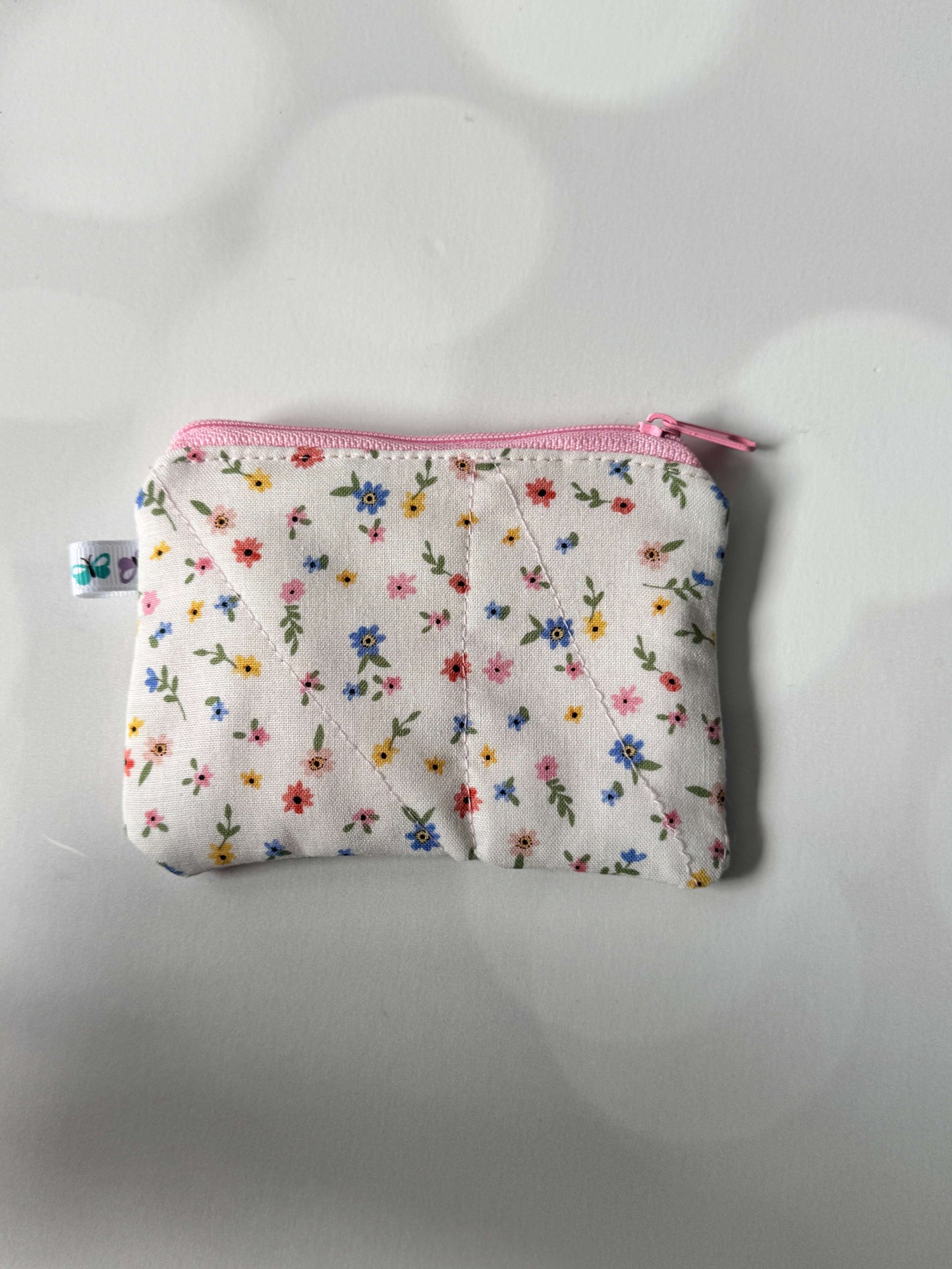 White floral coin wallet with a pink zipper, perfect for storing coins and small essentials.